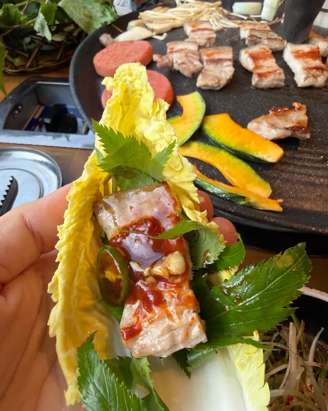 싱싱한 쌈 채소에 삼겹살과 쌈장을 얹어 쌈을 싸 먹는 모습