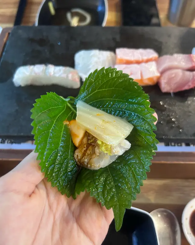 향긋한 깻잎에 백김치, 고추, 마늘을 곁들여 숙성회를 싸 먹는 모습