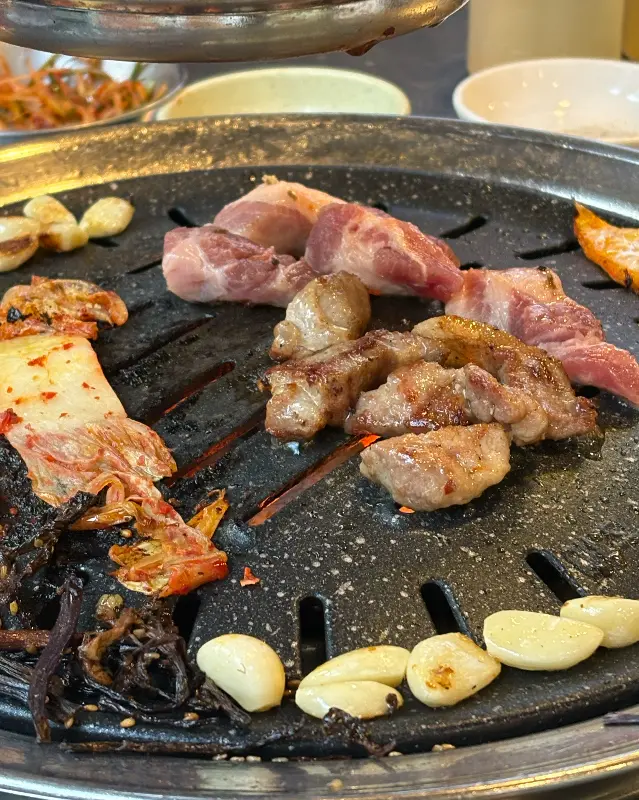 불판 위에 김치, 마늘과 함께 구워지는 삼겹살