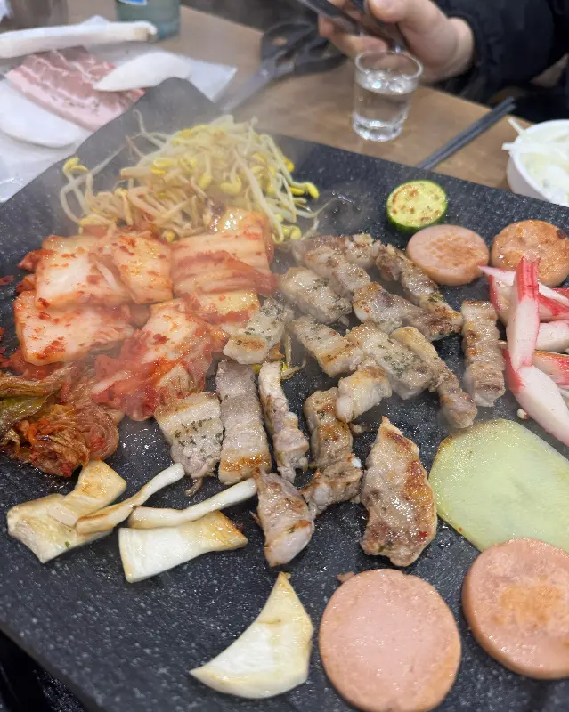 불판 가득 채워진 대패삼겹살과 김치, 콩나물