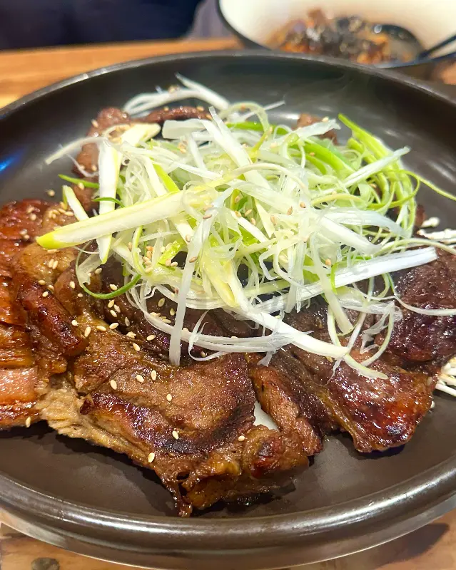 윤기가 흐르는 석갈비 위에 파채와 깨가 듬뿍 뿌려져 있다.