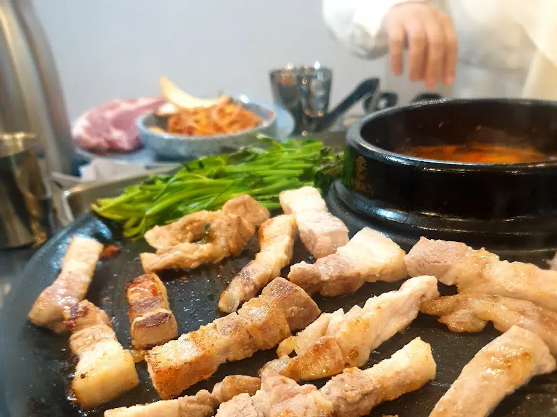 솥뚜껑에 구워진 삼겹살과 김치, 미나리