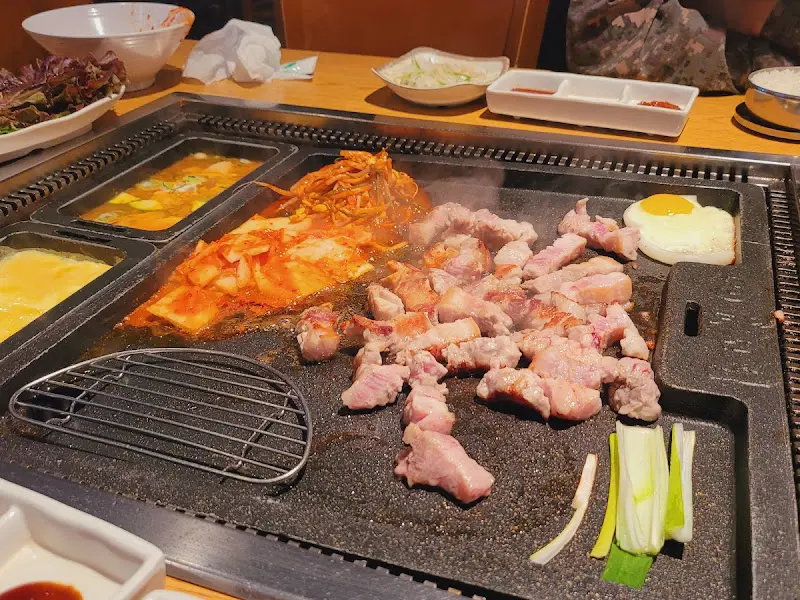 잘 구워진 삼겹살과 김치, 계란, 콩나물이 철판 위에 푸짐하게 놓여있는 모습