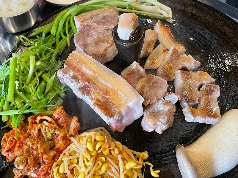 솥뚜껑 위에 푸짐하게 구워진 돼지고기와 곁들임 채소