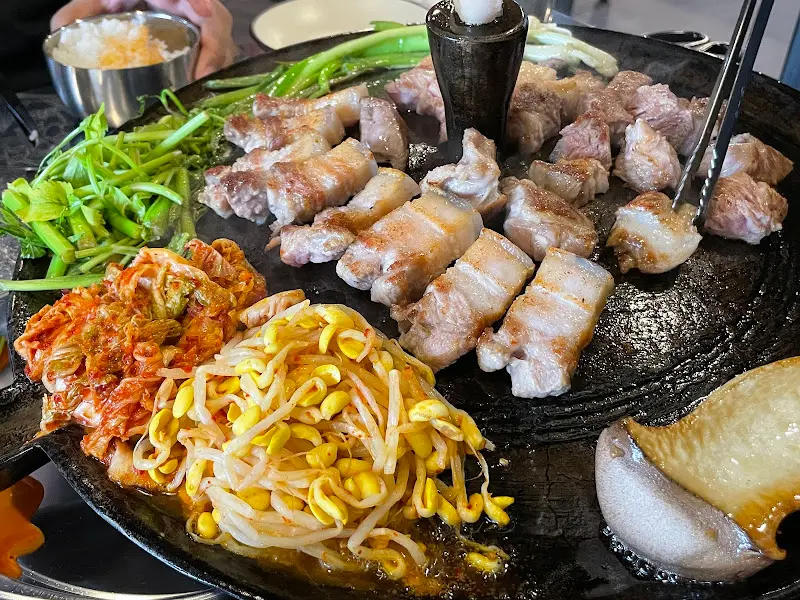 무쇠 솥뚜껑에 구워진 돼지고기를 쌈으로 즐기는 모습