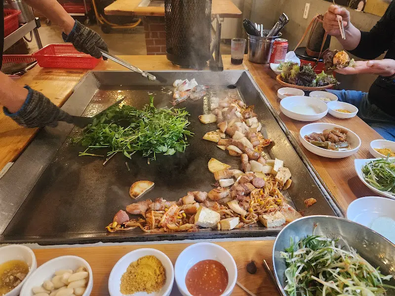 철판 위에서 삼겹살, 김치, 야채가 함께 구워지는 모습, 풍성한 식감을 자랑한다.