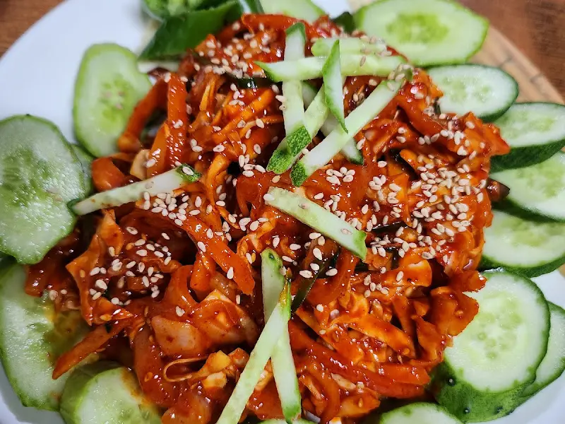 한치무침 위에 깨가 뿌려져 있고 주변에 오이가 놓여져 있어 신선함을 더하는 모습