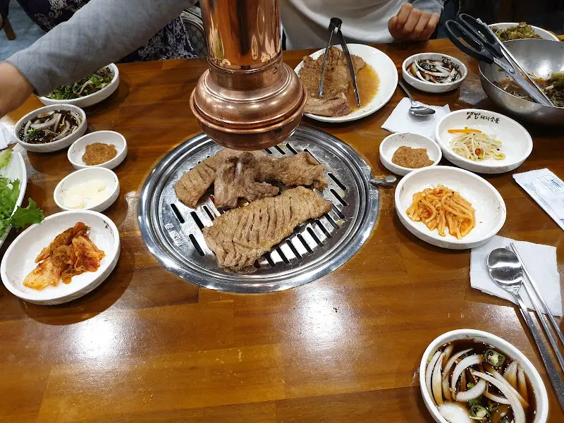 불판 위 초벌 갈비, 테이블 위에는 찌개와 다양한 곁들임 채소가 놓여있다.