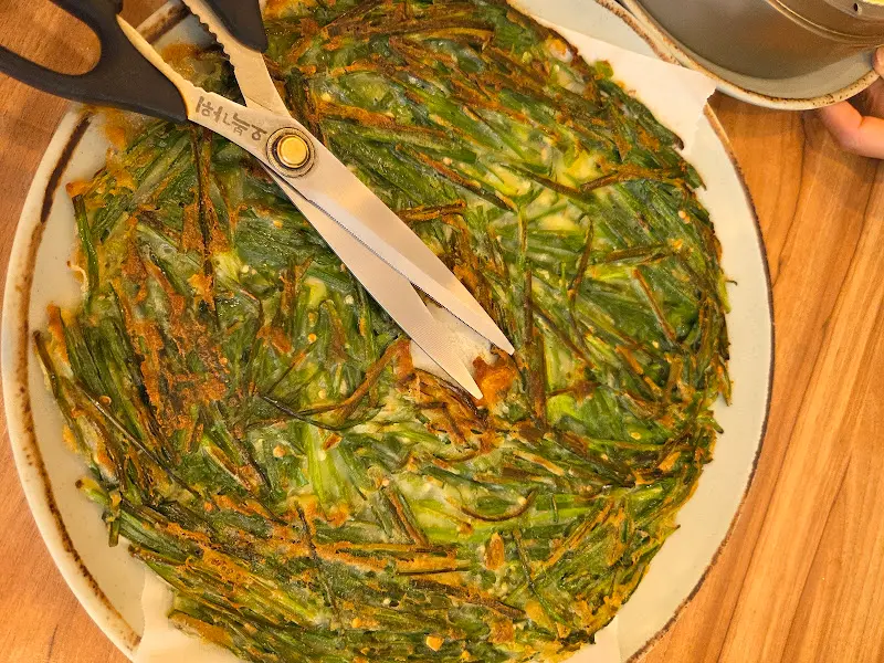 커다란 접시에 가득 담긴 땡초 부추전 위로 먹기 좋게 자를 수 있도록 가위가 놓여있다.