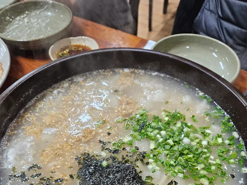 옹심이 칼국수가 담긴 뚝배기의 모습. 국물 위에 김 가루와 파가 뿌려져 있다.