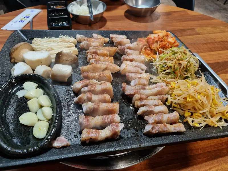불판 위에서 맛있게 익어가는 삼겹살과 채소들