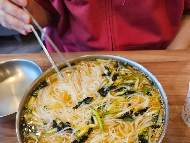 스테인리스 그릇에 담긴 콩국수를 젓가락으로 들어올리고 있는 모습이다.