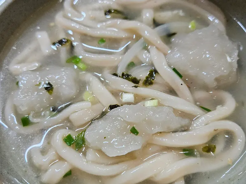 옹심이 칼국수가 담긴 그릇의 모습. 옹심이와 면이 국물에 잠겨 있고, 파와 김 가루가 뿌려져 있다.