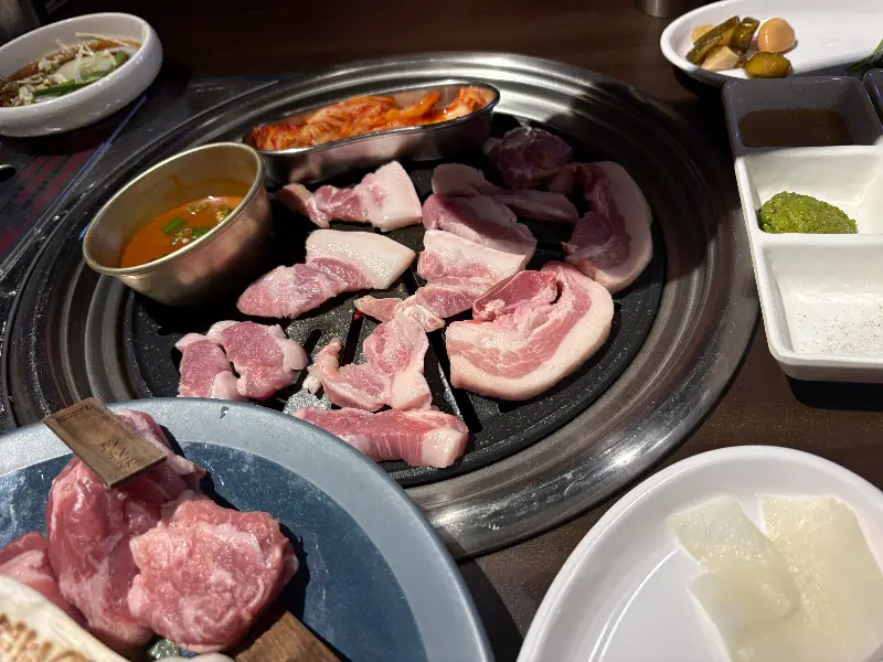 불판 위에 올려진 삼겹살과 다양한 소스