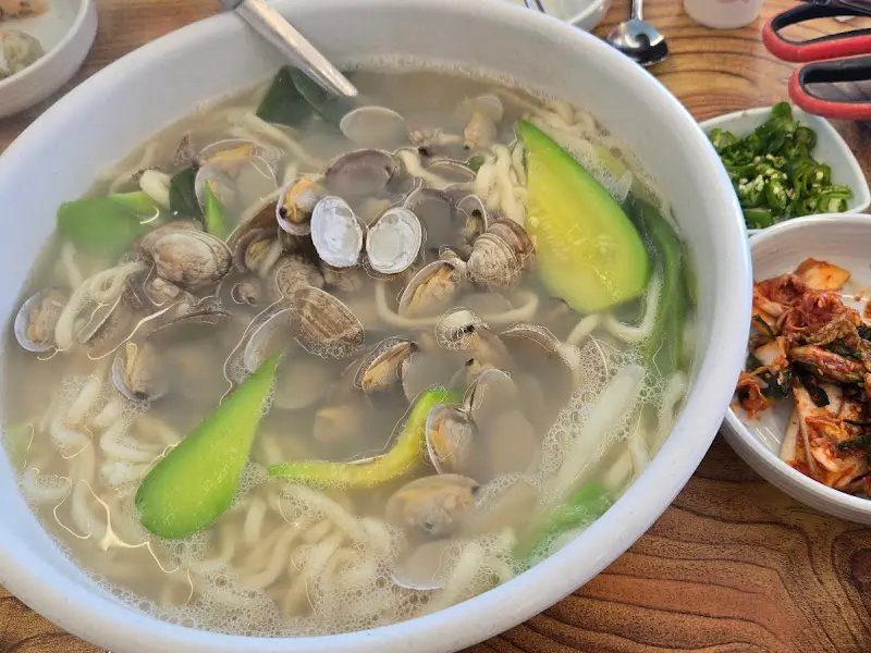 바지락 칼국수 한 그릇, 김치와 고추가 함께 놓여 있다.