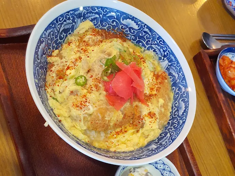 계란 옷을 입은 돈까스가 밥 위에 얹어진 돈까스 덮밥의 모습. 붉은 생강과 파슬리 가루가 고명으로 올라가 있다.