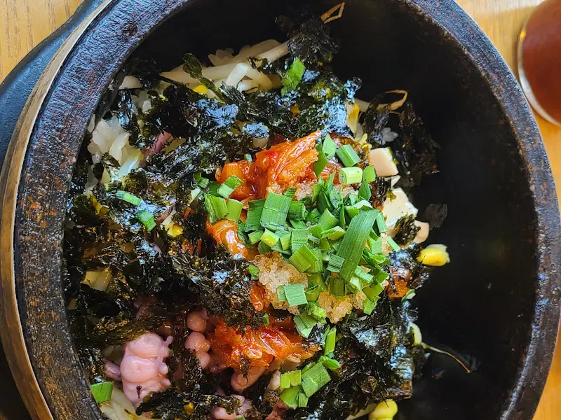 돌솥 안에서 조화롭게 어우러진 밥, 바지락, 채소, 김 가루, 그리고 양념장의 모습