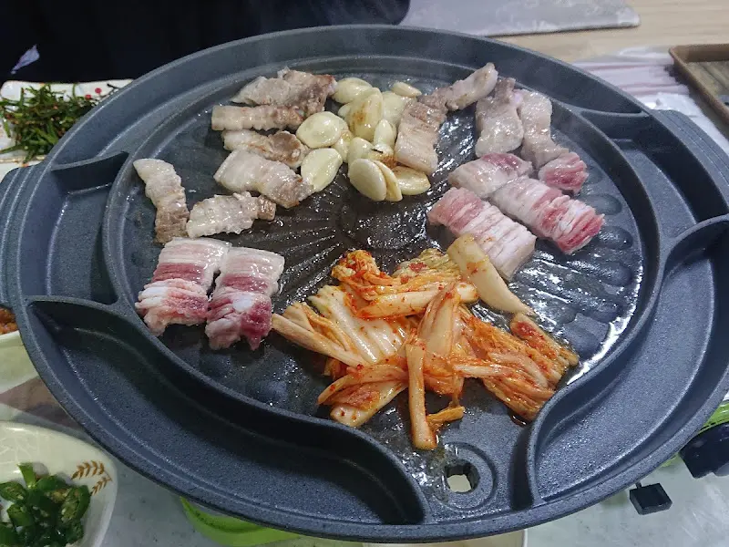불판 위에서 맛있게 구워지고 있는 삼겹살과 김치의 모습