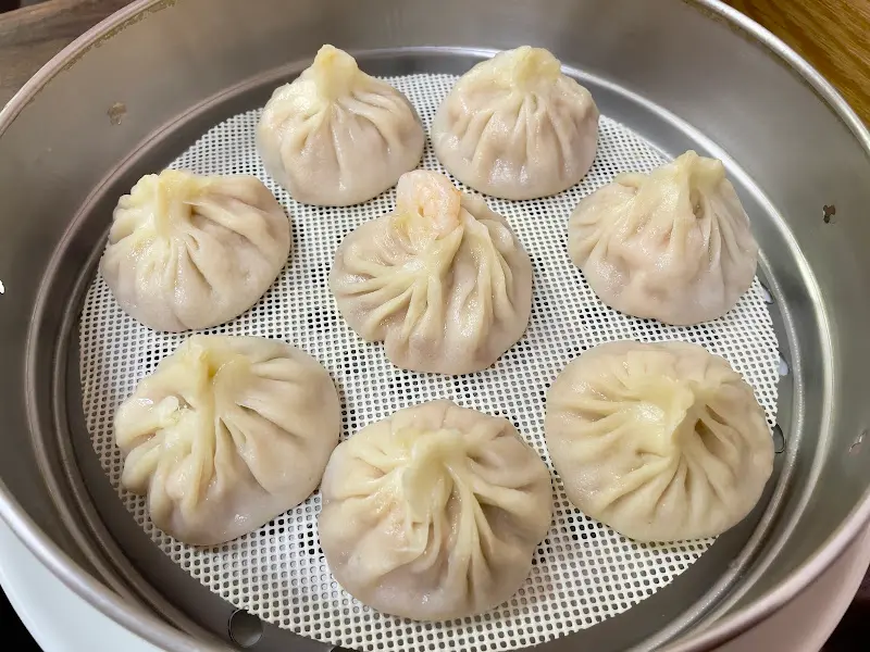 찜기에 담긴 새우 만두는 윗부분이 꽃처럼 오므려져 있으며, 만두피 너머로 분홍색 새우 살이 비쳐 보인다.