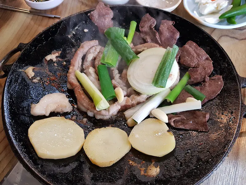 불판 위에 곱창, 대창, 막창, 양파, 감자, 마늘, 부추 등이 함께 구워지고 있는 모습