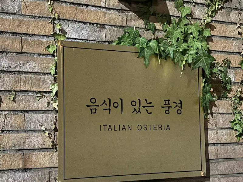 벽돌 벽에 걸린 '음식이있는풍경' 간판 사진. 담쟁이 덩굴이 간판을 감싸고 있다.