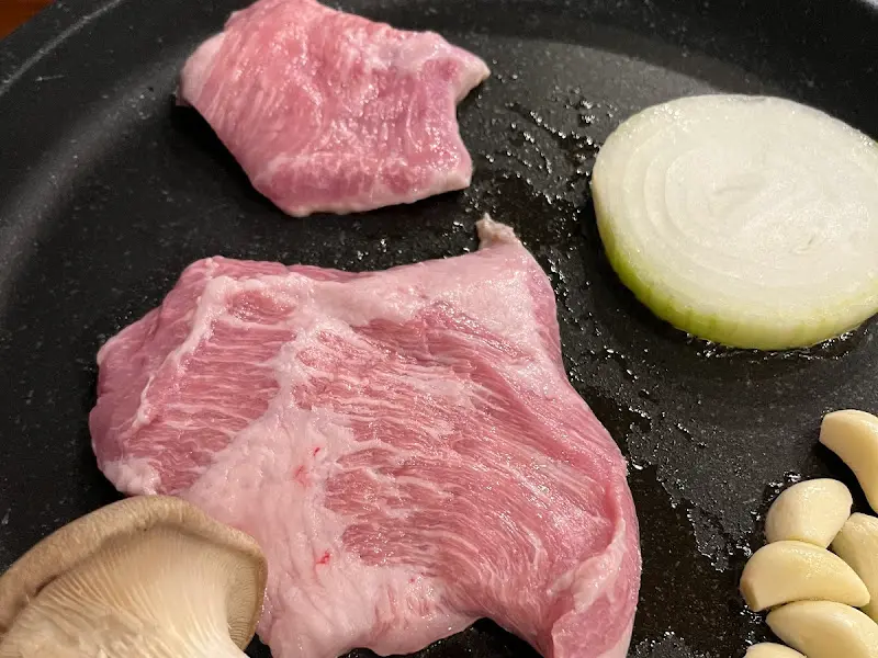 불판 위에서 익어가는 삼겹살, 양파, 마늘