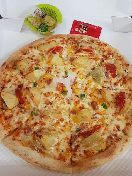 파인애플, 햄, 고추 등이 토핑된 피자의 모습. 중앙에는 피자를 고정하는 흰색 플라스틱 지지대가 놓여 있다.