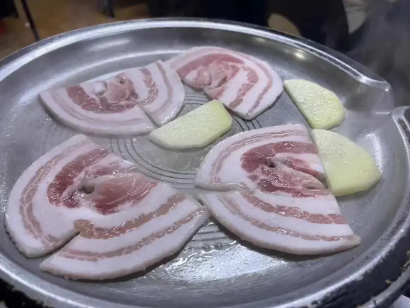 불판 위에서 익어가는 냉동 삼겹살과 감자