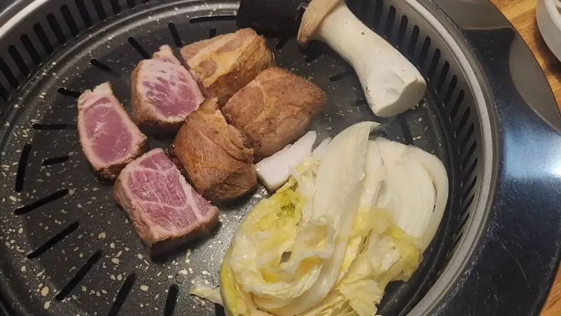 불판 위에서 목살, 버섯, 꽈리고추 등이 구워지고 있는 모습