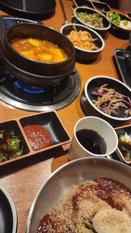 테이블 위에 김치찌개, 멜젓, 각종 반찬 등이 푸짐하게 차려진 모습