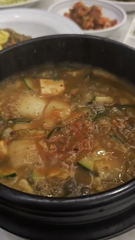 검은색 뚝배기에 담긴 된장찌개는 김이 모락모락 피어오르고, 깍둑썰기한 두부와 애호박이 넉넉하게 들어있어 푸짐함을 더합니다.