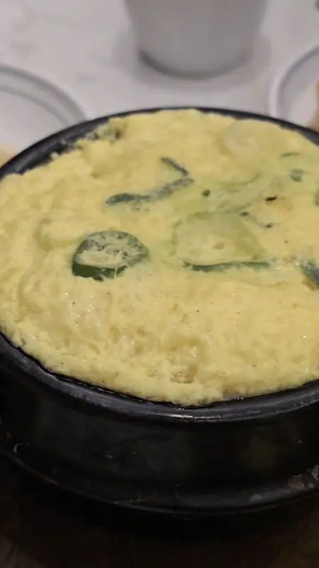 검은색 뚝배기에 담긴 계란찜은 부드럽고 촉촉해 보이며, 찜기에서 갓 꺼낸 듯 따뜻한 김이 살짝 올라오고 있습니다.