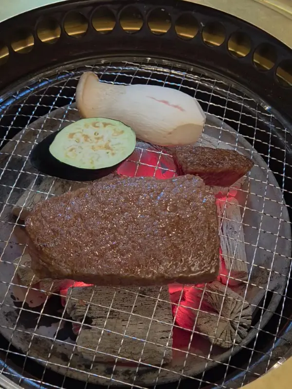 숯불 위 석쇠에서 한우가 지글거리는 모습은 식욕을 자극하고, 곁들여진 큼지막한 새송이버섯과 가지는 풍성함을 더합니다.