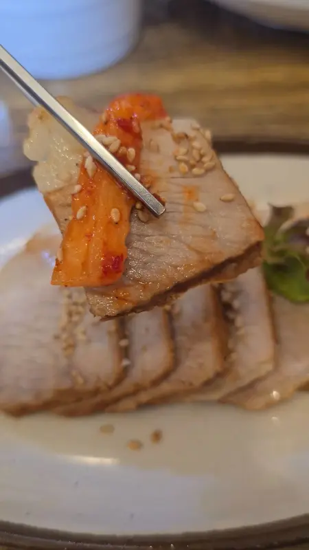 윤기가 흐르는 수육 한 점을 젓가락으로 집어올리는 모습