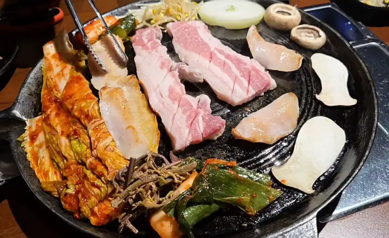 솥뚜껑 위에 삼겹살, 김치, 버섯 등이 푸짐하게 올려져 있는 모습