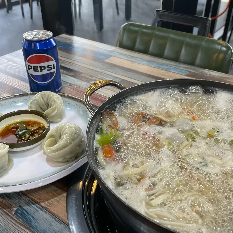 해물칼국수와 함께 놓인 만두 접시와 음료수 캔