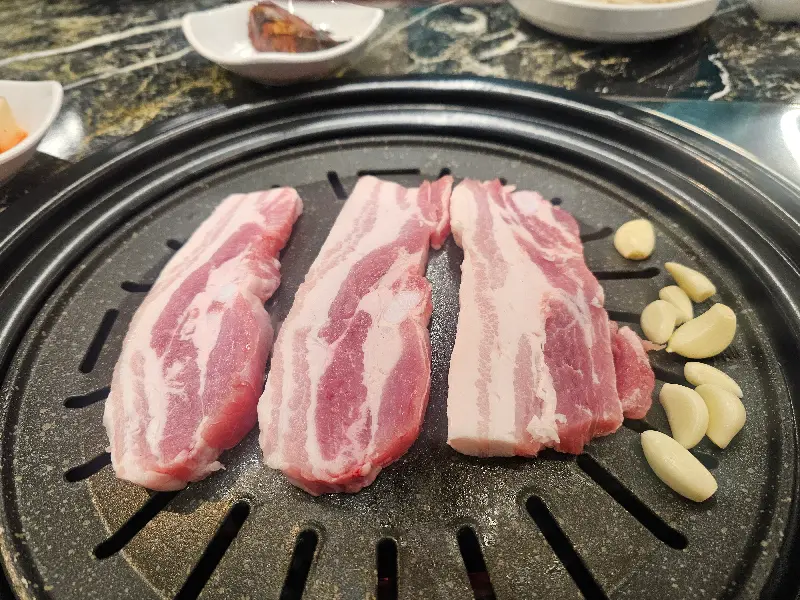 불판 위에 가지런히 놓인 삼겹살과 마늘