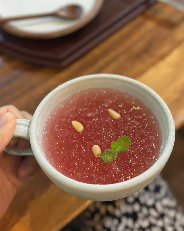 붉은 빛깔의 오미자차에 잣과 민트 잎이 올려진 모습