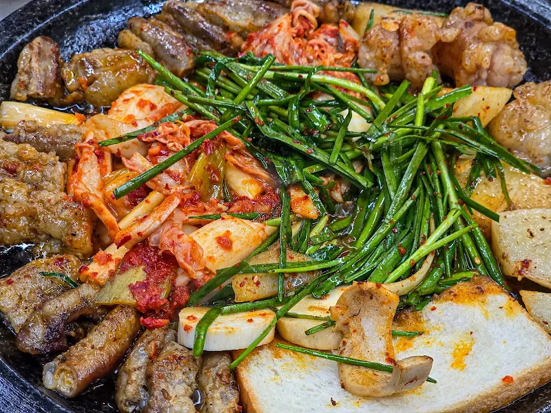 돌판 위에 곱창, 대창, 김치, 부추, 양파, 버섯이 푸짐하게 담겨 있는 모습