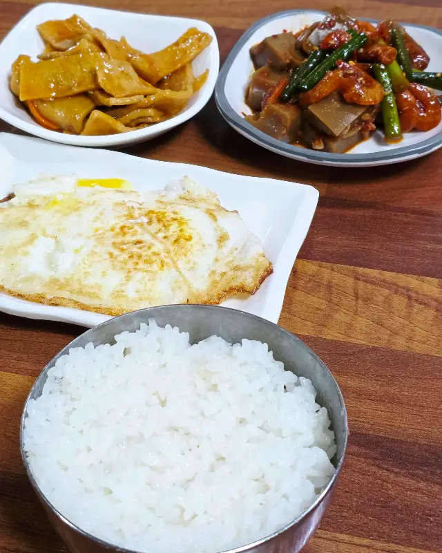 푸짐한 밑반찬과 계란후라이, 갓 지은 흰 쌀밥 한 공기가 놓인 테이블 사진