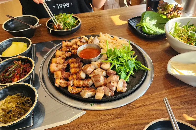 잘 익은 삼겹살을 다양한 밑반찬과 함께 즐기는 모습