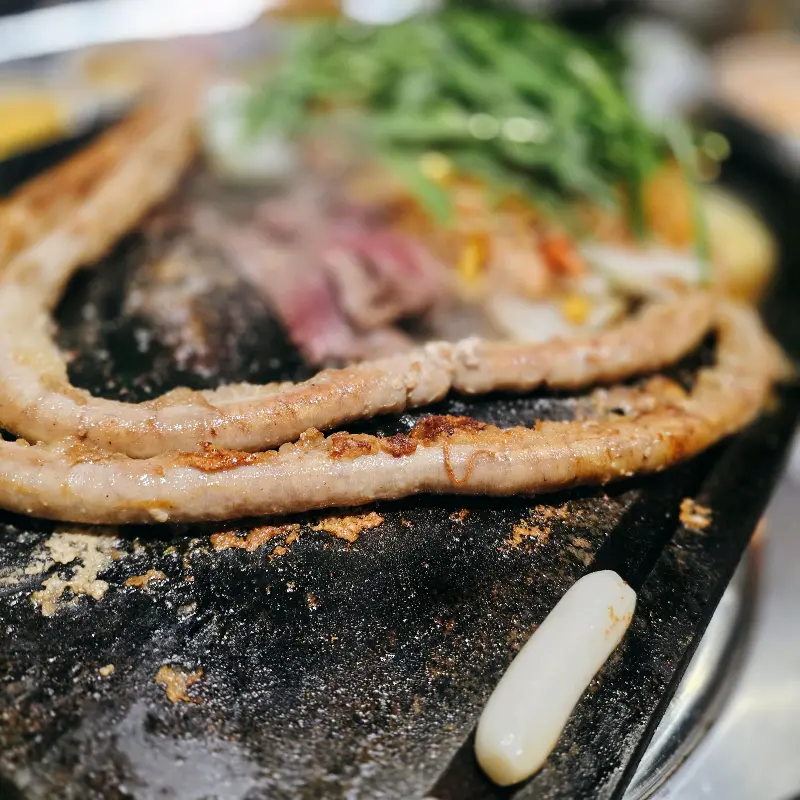 돌판 위에 노릇하게 구워진 대창의 클로즈업 샷