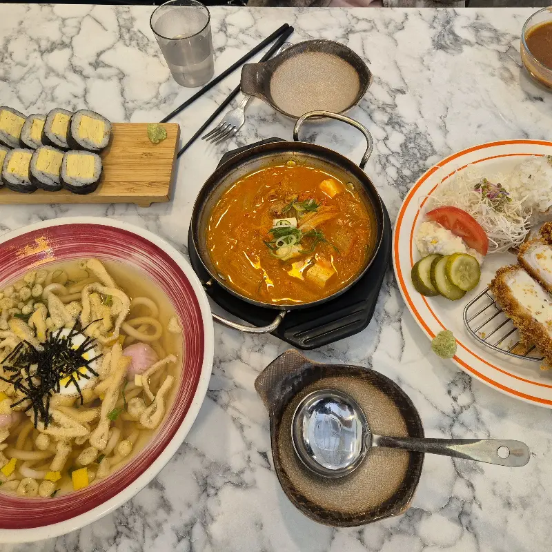 돈까스, 김치찌개, 계란 김밥이 놓인 테이블 전경