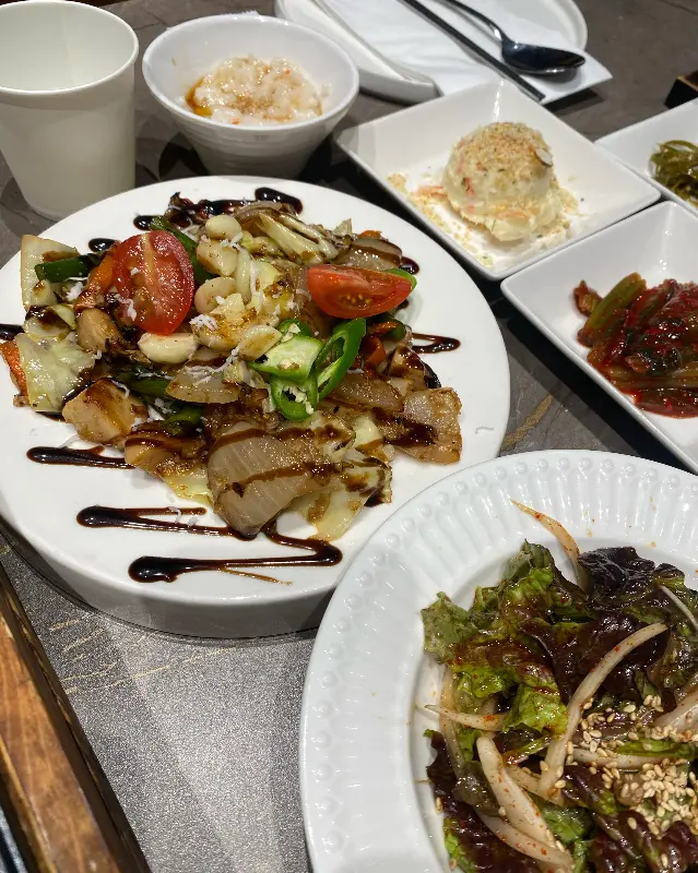 테이블 위에 삼겹살과 다양한 밑반찬이 놓여 있다.