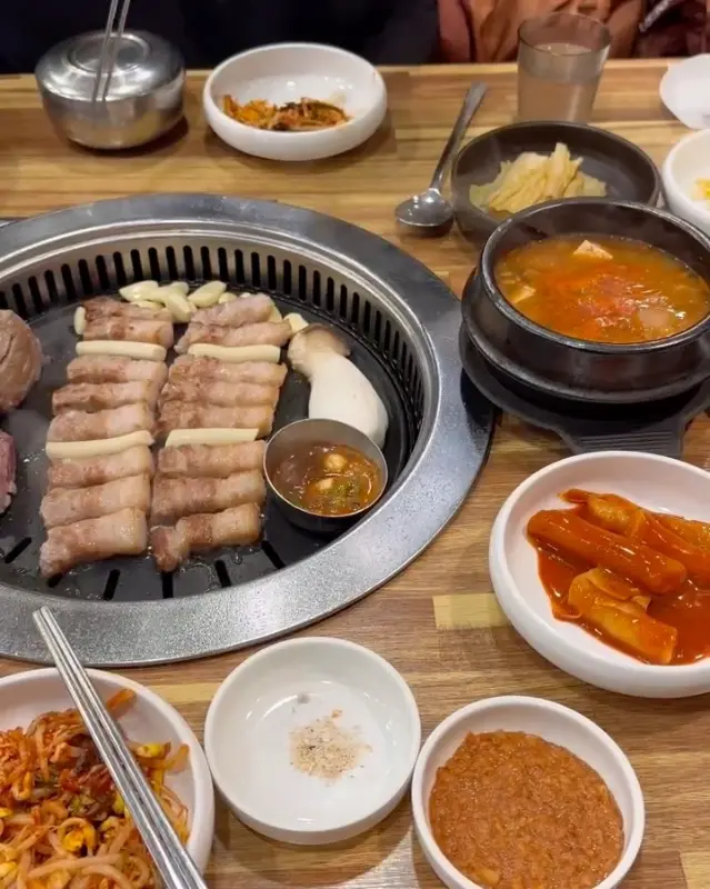 불판 위에 삼겹살, 떡, 버섯 등이 함께 구워지고 있는 모습