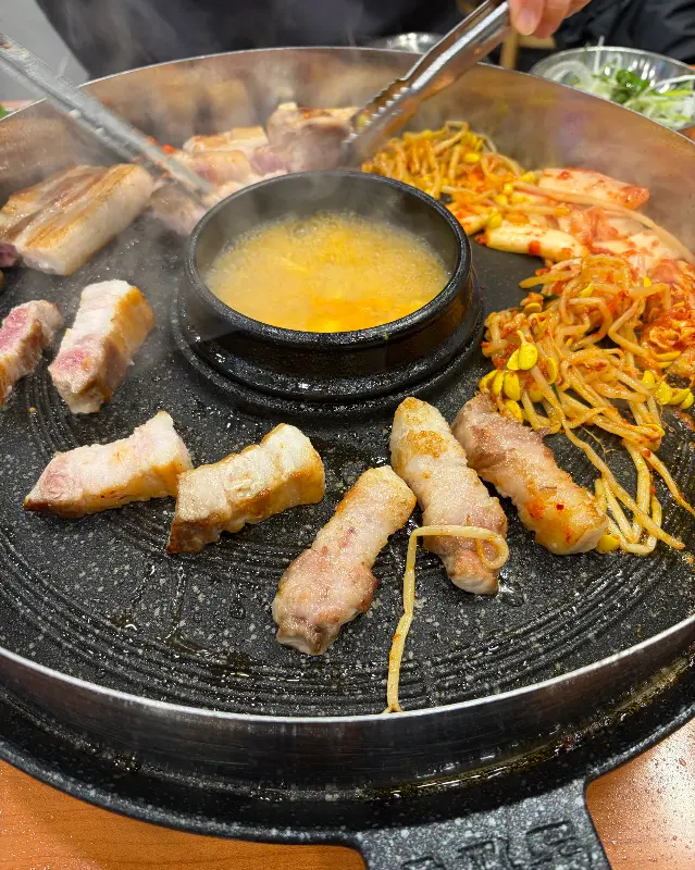 솥뚜껑에 삼겹살, 김치, 콩나물, 떡이 구워지는 모습