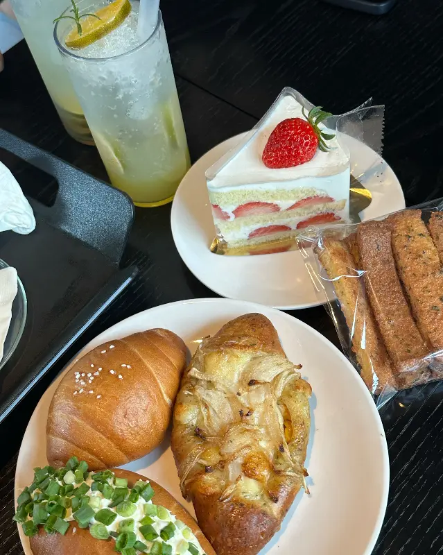 테이블 위에 놓인 빵과 음료. 창녕 양파빵과 딸기 케이크, 에이드가 보인다.