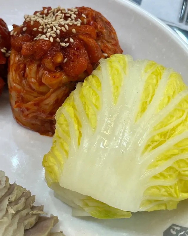 싱싱한 배추에 보쌈과 김치를 올려 한입 가득 싸 먹는 모습