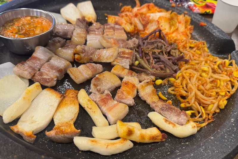 불판 위 삼겹살, 김치, 떡, 버섯