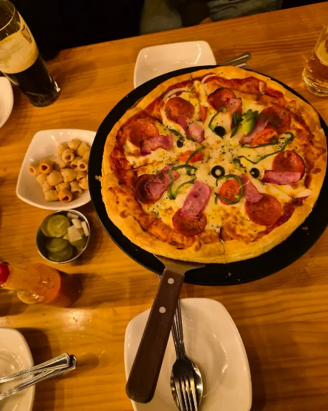 테이블 위에 놓인 피자와 맥주, 소스 등의 모습